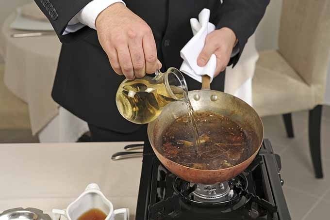 Person pours liquid into a browned pan on a portable burner